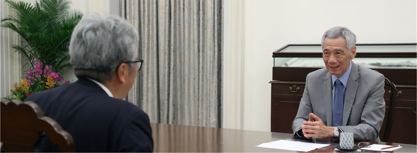 Two people sit at a table; Lee Hsien Loong in a suit.